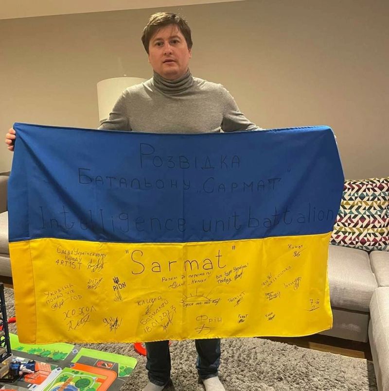Paul Ryazanov holding a Ukrainian flag signed by members of the Sarmat intelligence unit battalion